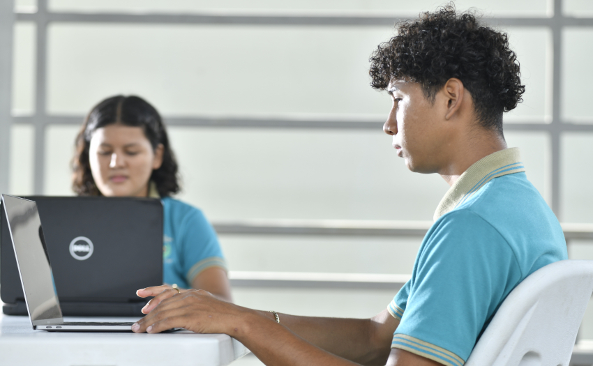 Dos estudiantes adolescentes, mujer y hombre, frente a computadoras. 