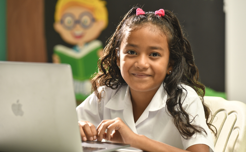 Niña con uniforme de escuela, sentada, con una computadora. 