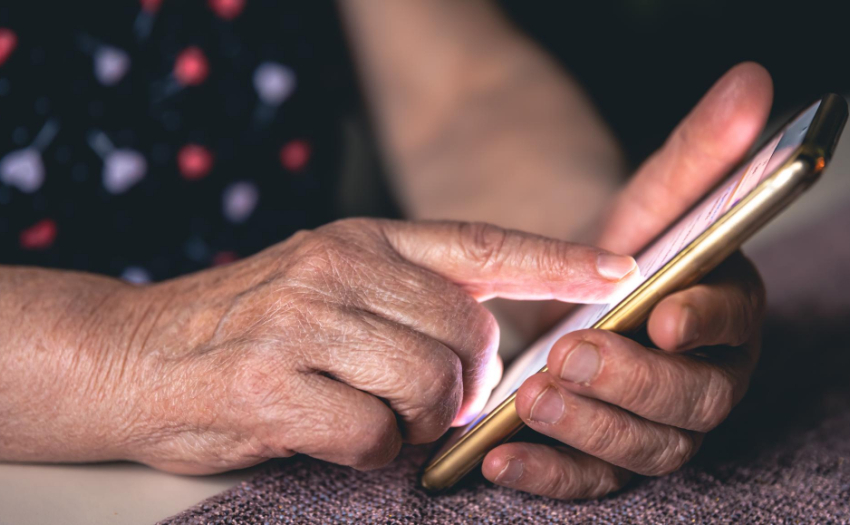 Manos de mujer adulta mayor sosteniendo y usando un celular. 