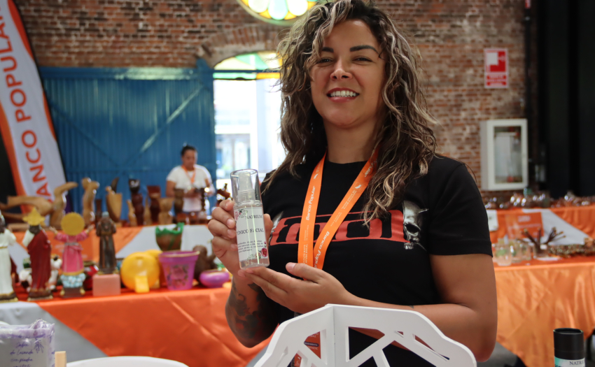 Emprendedora apoyada por IMAS Impulsa, en la feria del 2025. Mira hacia la cámara, sonríe y muestra uno de sus productos. 