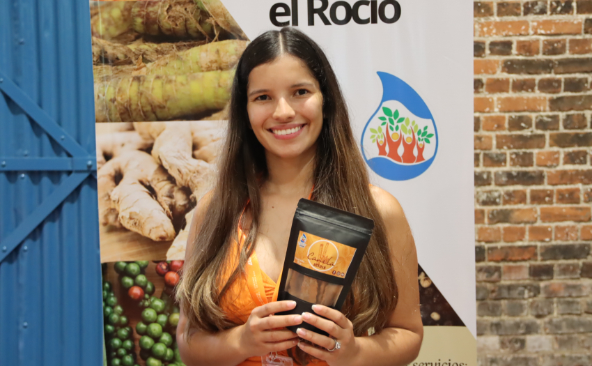 Emprendedora participante en la primera Feria IMAS Impulsa, del 2025. Mira hacia la cámara y sonríe. Muestra uno de los productos que vende. 