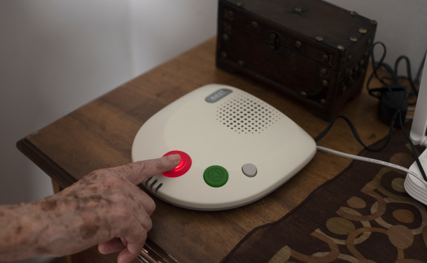 Imagen de mano de adulta mayor en intercomunicador ilustrando servicio de tele asistencia.