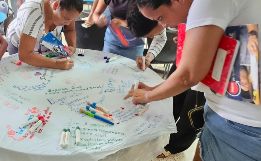 Personas participantes de la Feria Vocacional de la ULDS Chomes durante una actividad. Escriben en un mantel de una mesa. 