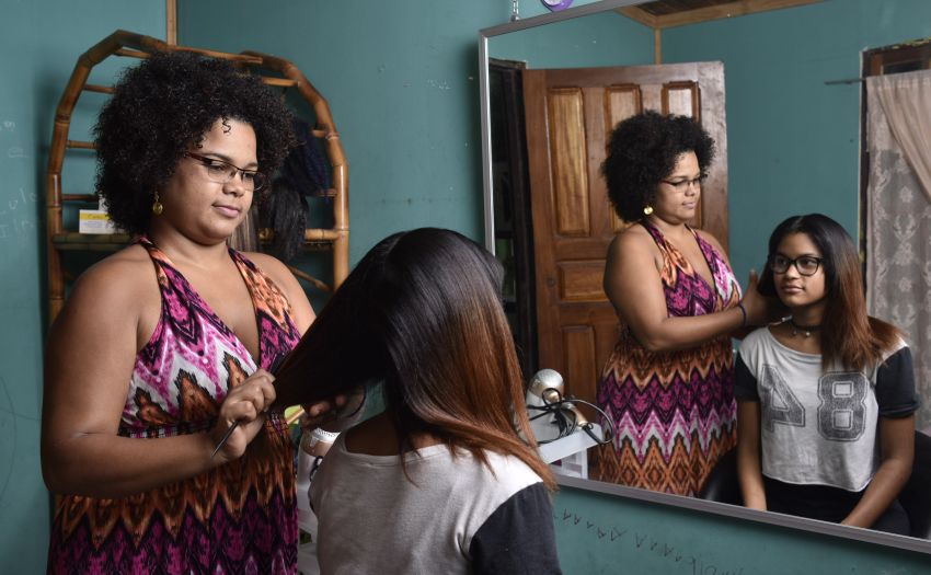 Mujer beneficiaria del IMAS peina a niña frente a un espejo. 