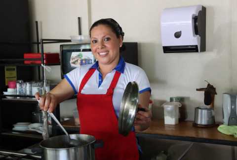 Emprendedora beneficiaria del IMAS. Está en su soda, coloca una cuchara en una olla.